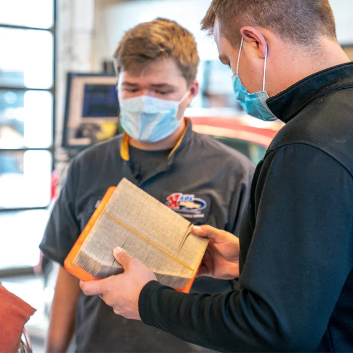Automotive technicians inspecting a vehicle engine air filter during maintenance service.